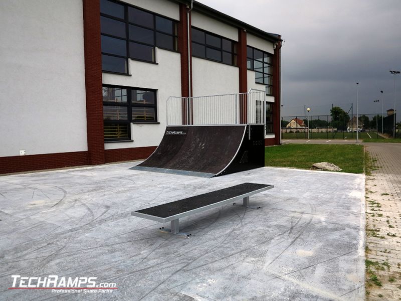 Grindbench and quarter pipe on a concrete flat and a grass in the background