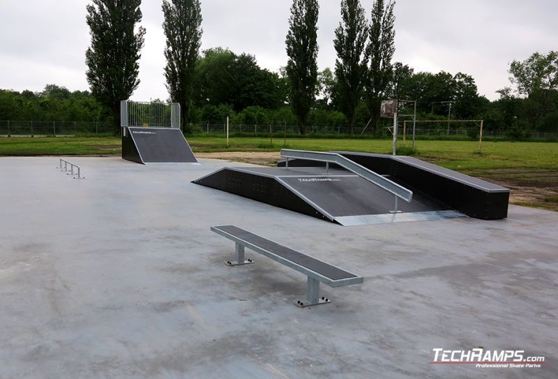 Urządzenia skateparku umieszczone na betonowym placu wśród zieleni