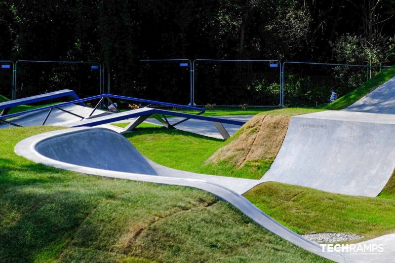 Ogólny widok na skatepark z falistym snakerunem i różnorodnymi przeszkodami betonowymi